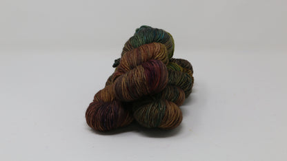 3 skeins of hand-dyed yarn in earthy, variegated shades of green, brown, and burgundy, displayed on a white surface and background.