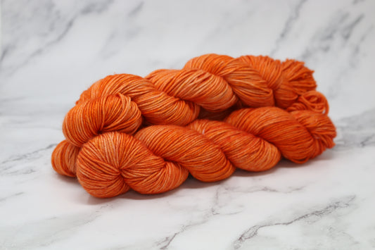 Three skeins of tonal bright orange yarn on a white marble surface