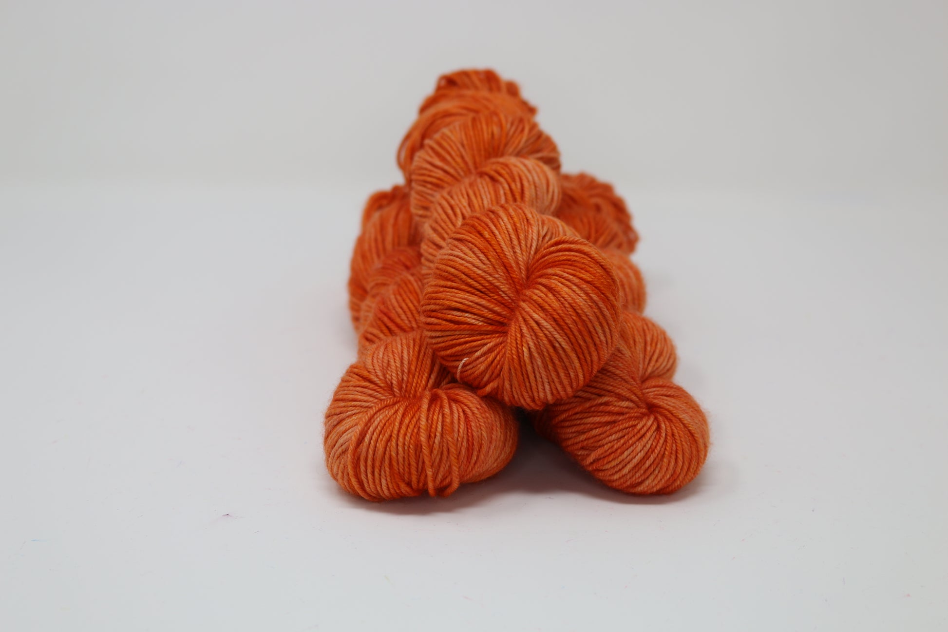 Three skeins of tonal bright orange yarn on a white surface
