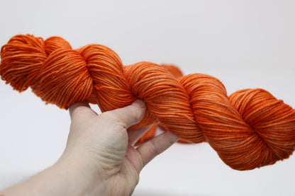 A skein of bright orange yarn held by a person's left hand in front of a white background