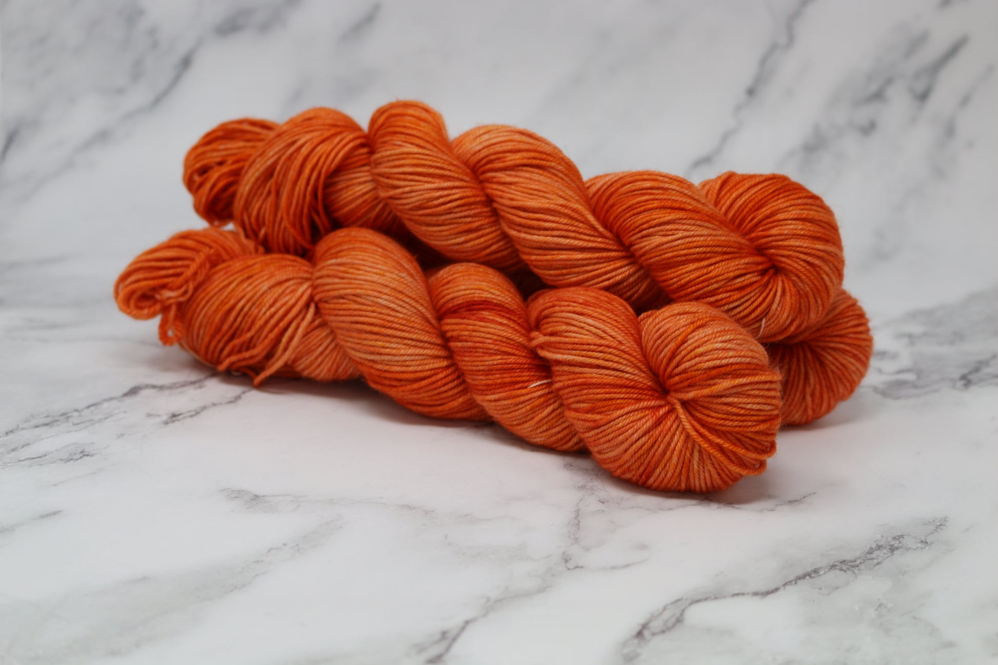 Three skeins of tonal bright orange yarn on a white marble surface
