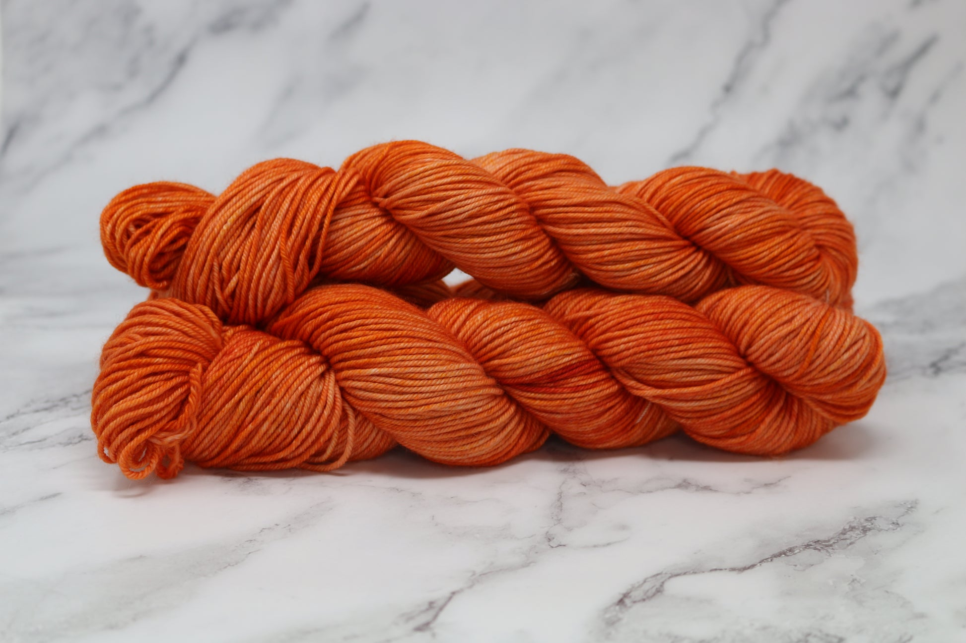 Three skeins of tonal bright orange yarn on a white marble surface