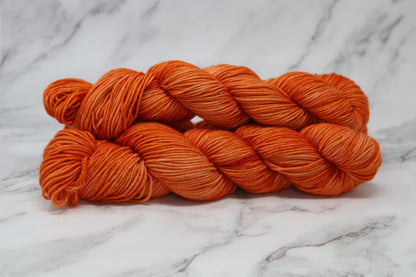 Three skeins of tonal bright orange yarn on a white marble surface