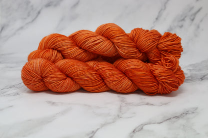 Three skeins of tonal bright orange yarn on a white marble surface
