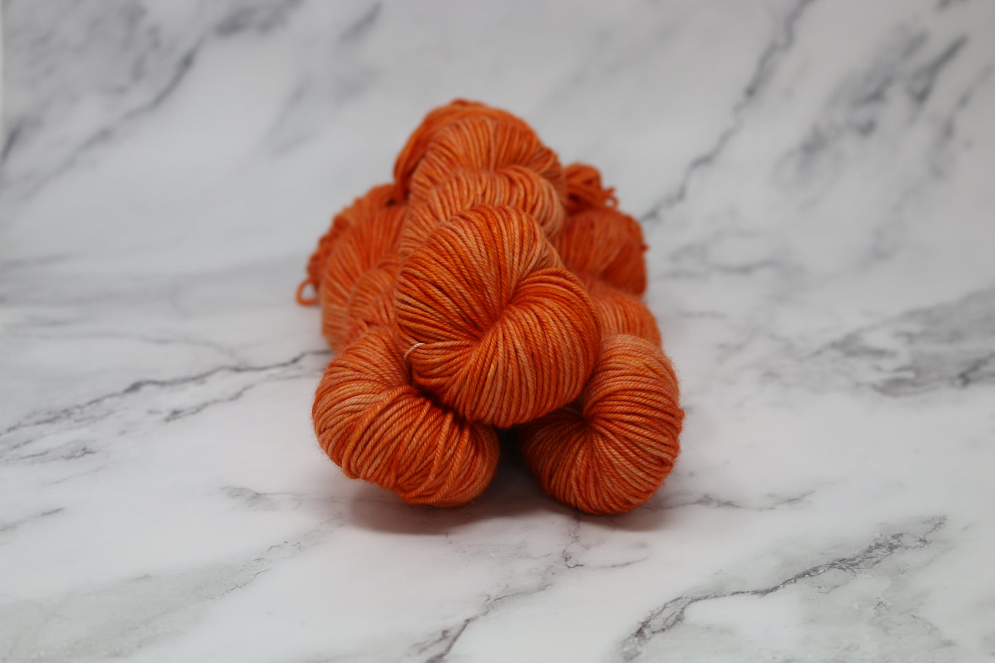 Three skeins of tonal bright orange yarn on a white marble surface