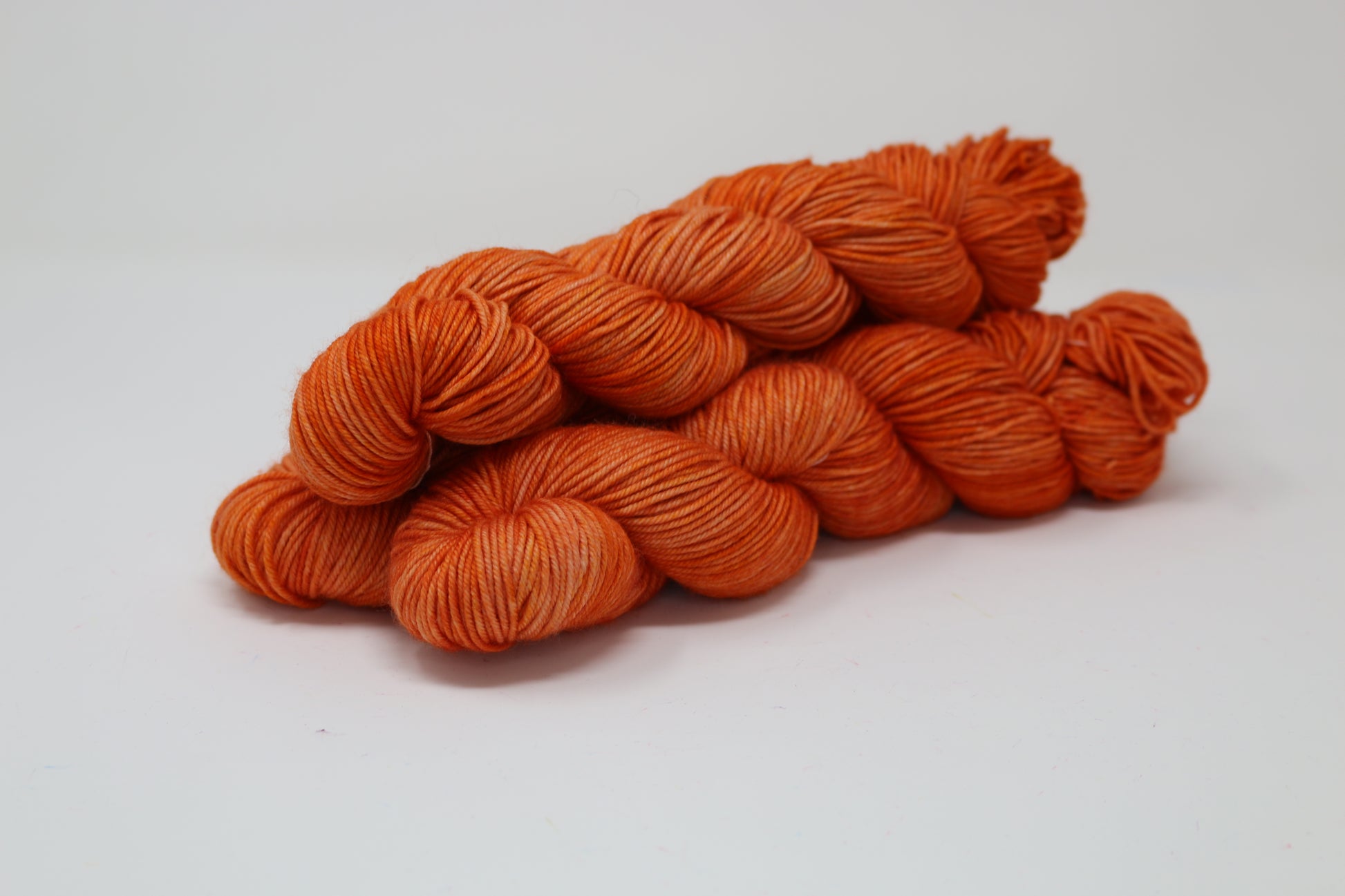Three skeins of tonal bright orange yarn on a white surface