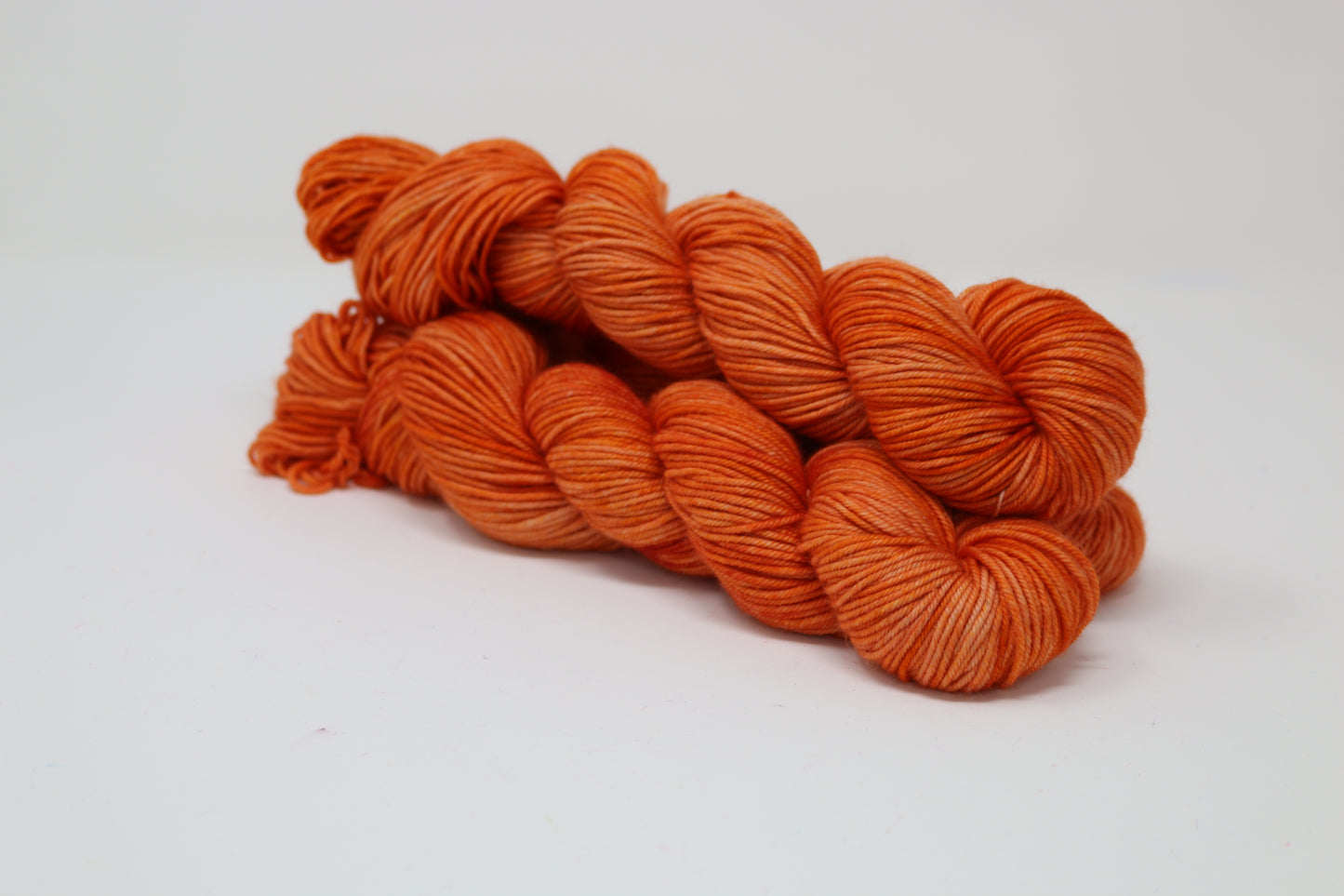 Three skeins of tonal bright orange yarn on a white surface