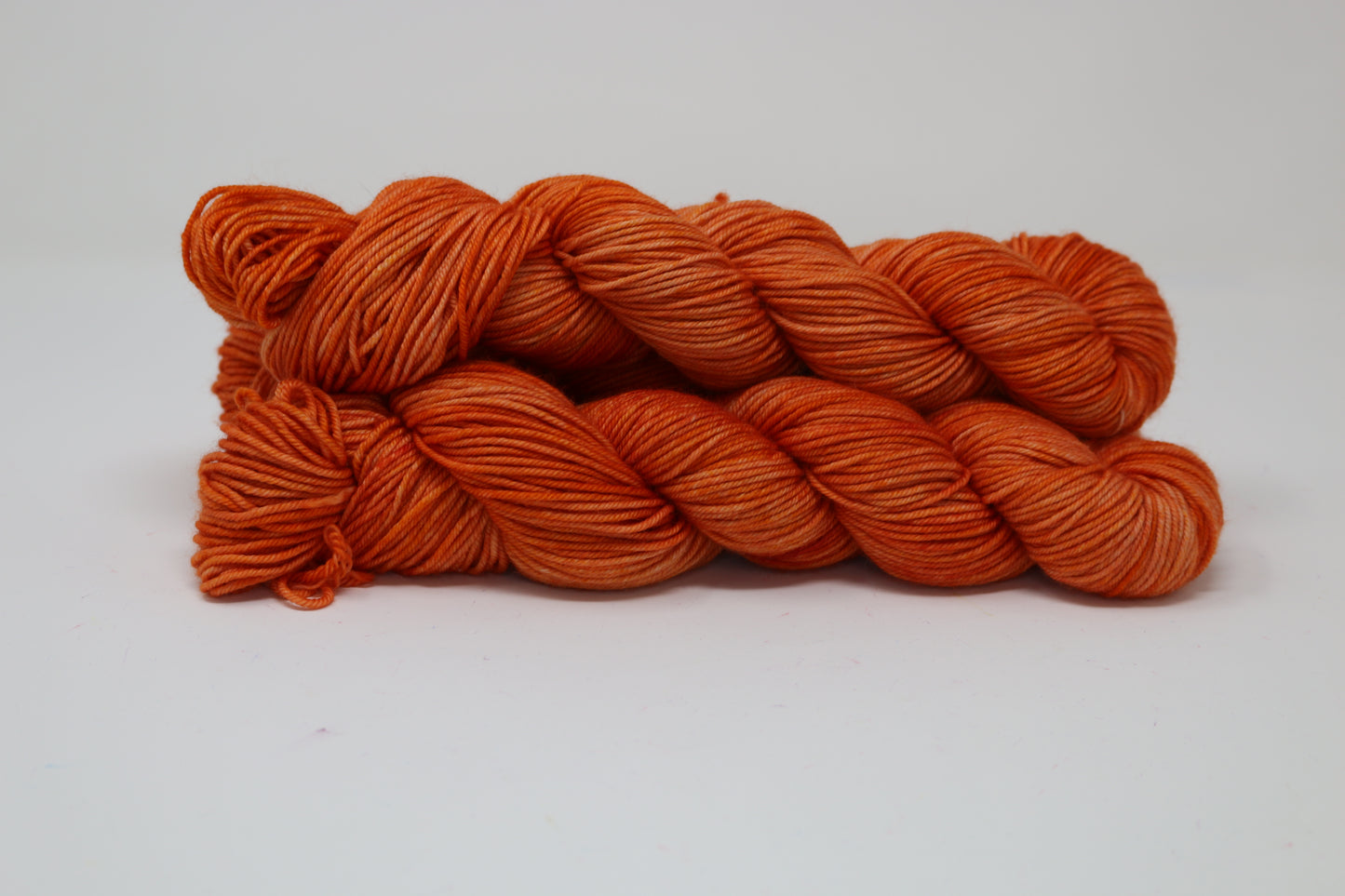 Three skeins of tonal bright orange yarn on a white surface