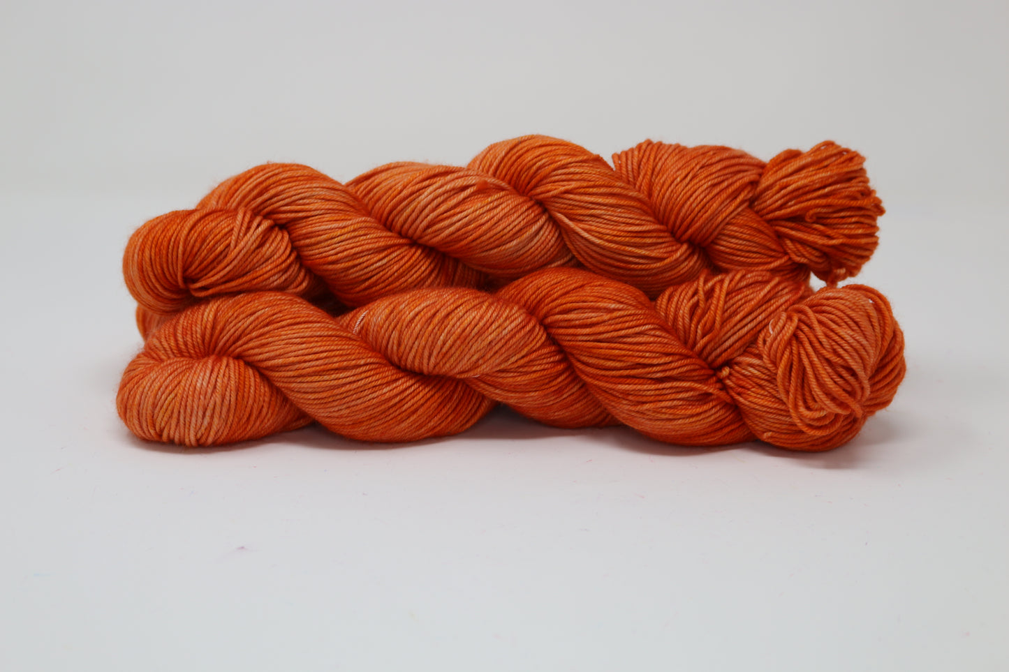 Three skeins of tonal bright orange yarn on a white surface