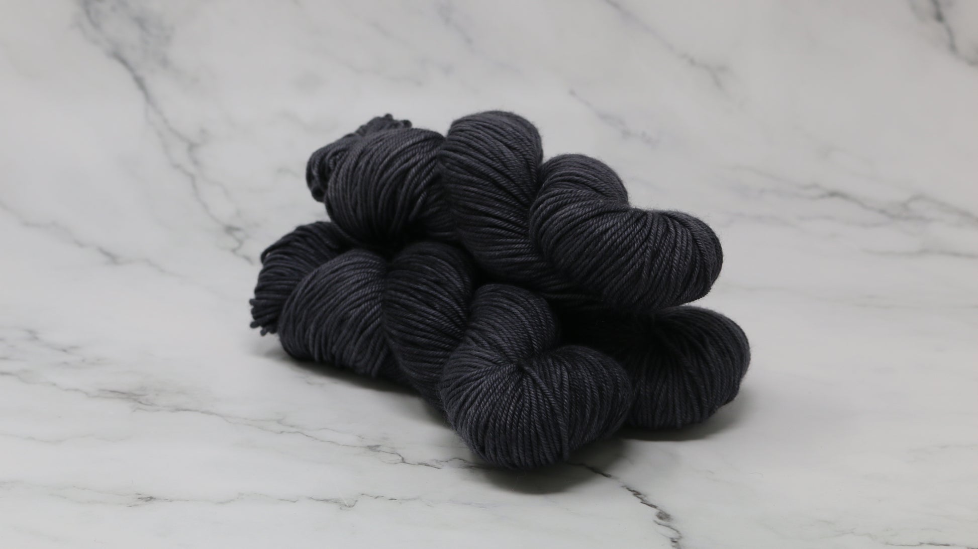 3 skeins of dark grey yarn on a marble surface and background