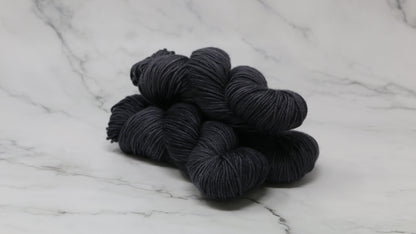 3 skeins of dark grey yarn on a marble surface and background