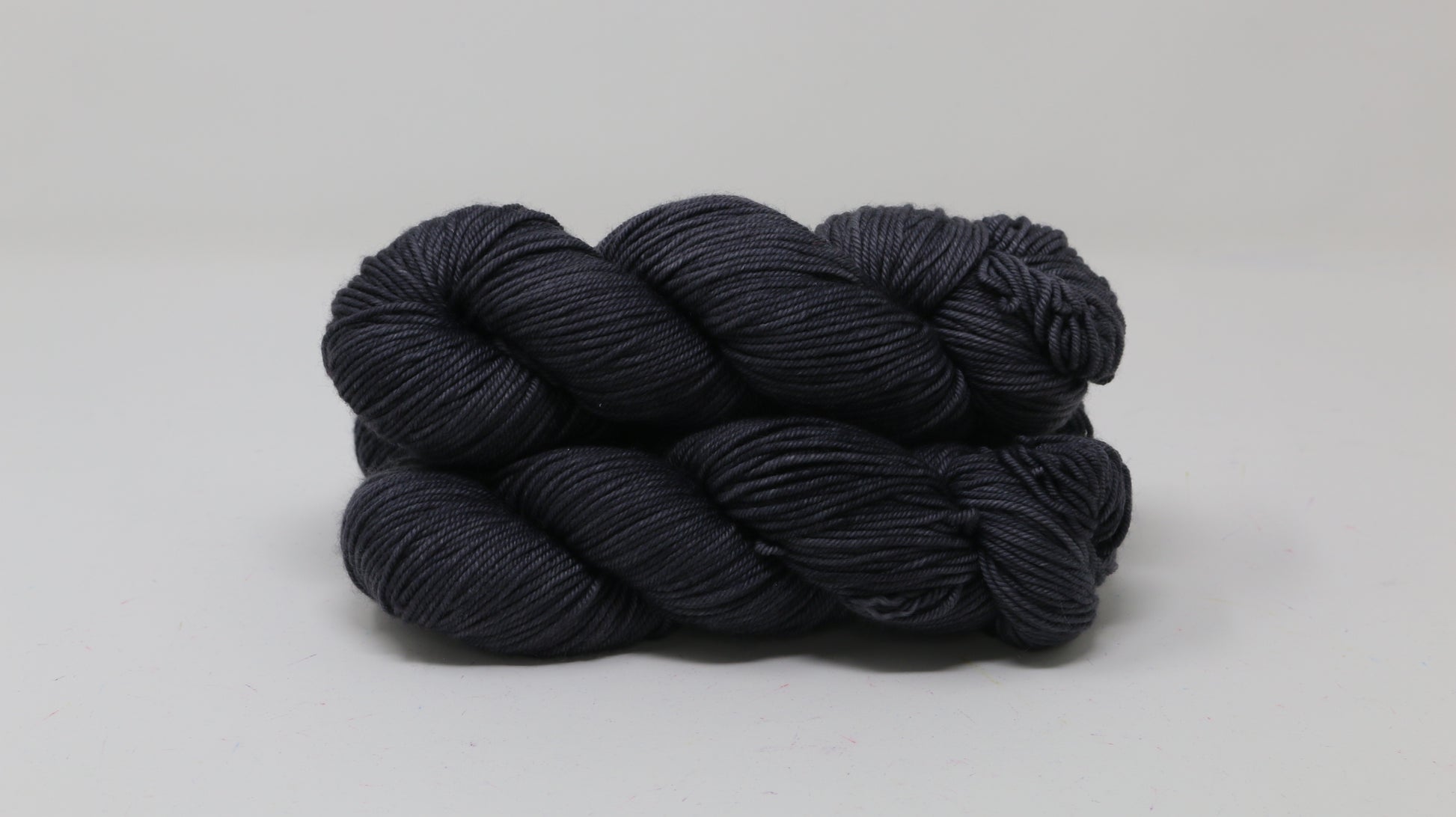 3 skeins of dark grey yarn on a white surface and background