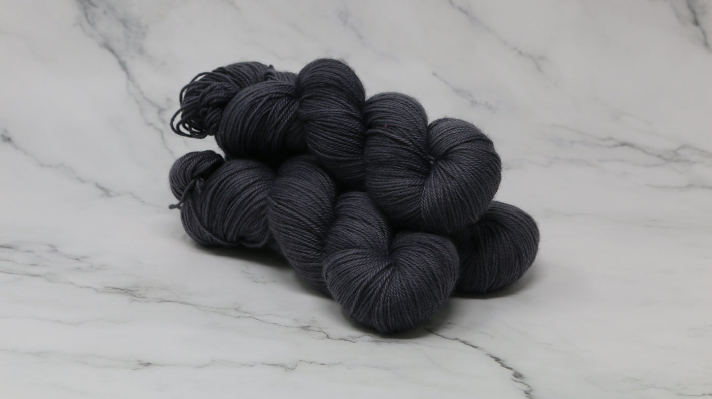3 skeins of dark grey yarn on a white marble surface and background
