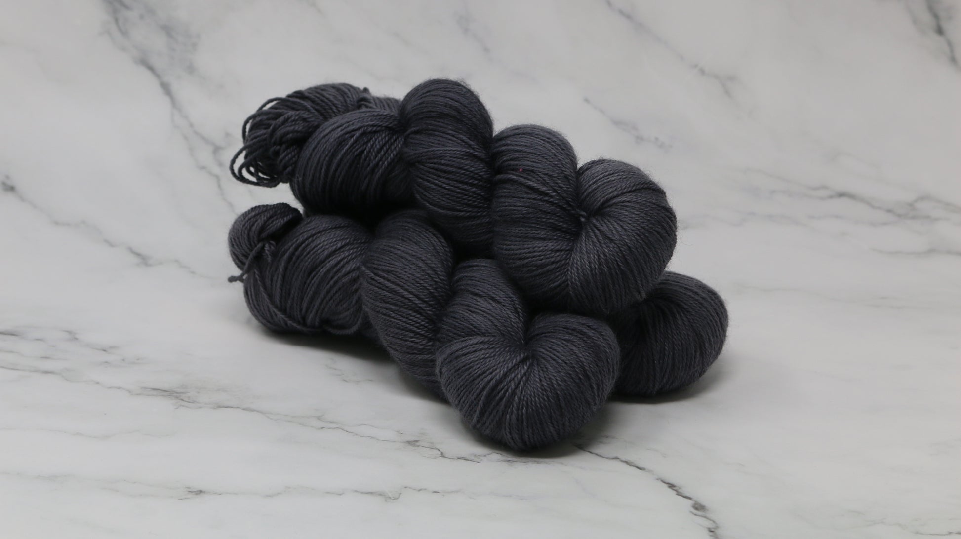 3 skeins of dark grey yarn on a white marble surface and background