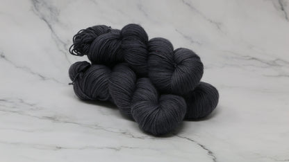 3 skeins of dark grey yarn on a white marble surface and background