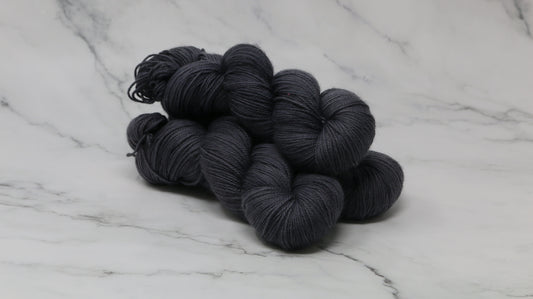 3 skeins of dark grey yarn on a white marble surface and background