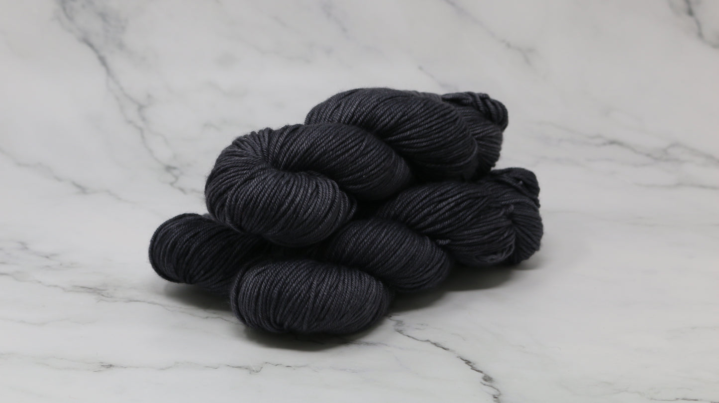 3 skeins of dark grey yarn on a marble surface and background