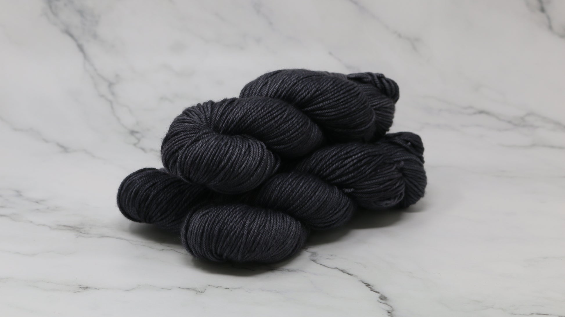 3 skeins of dark grey yarn on a marble surface and background
