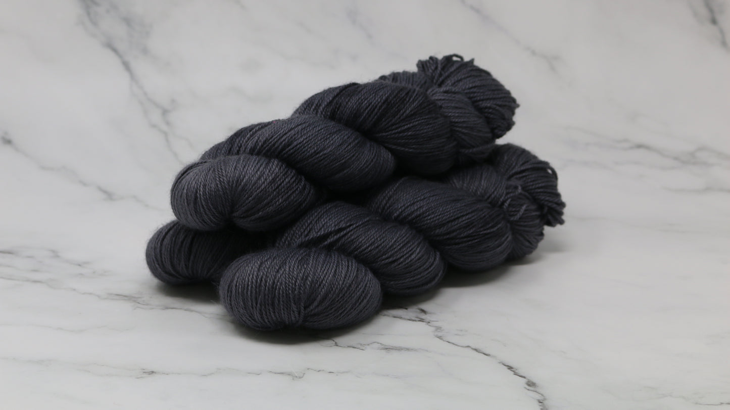 3 skeins of dark grey yarn on a white marble surface and background