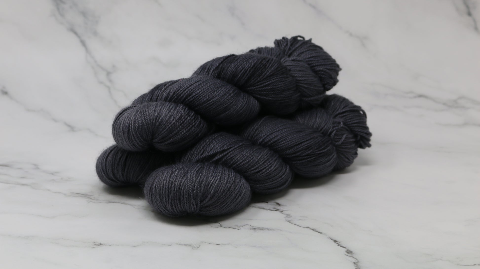 3 skeins of dark grey yarn on a white marble surface and background