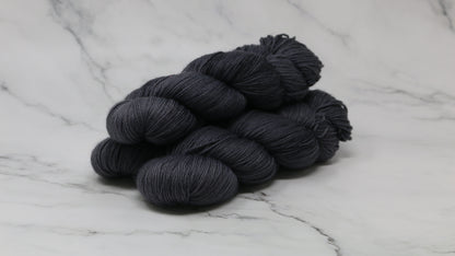 3 skeins of dark grey yarn on a white marble surface and background