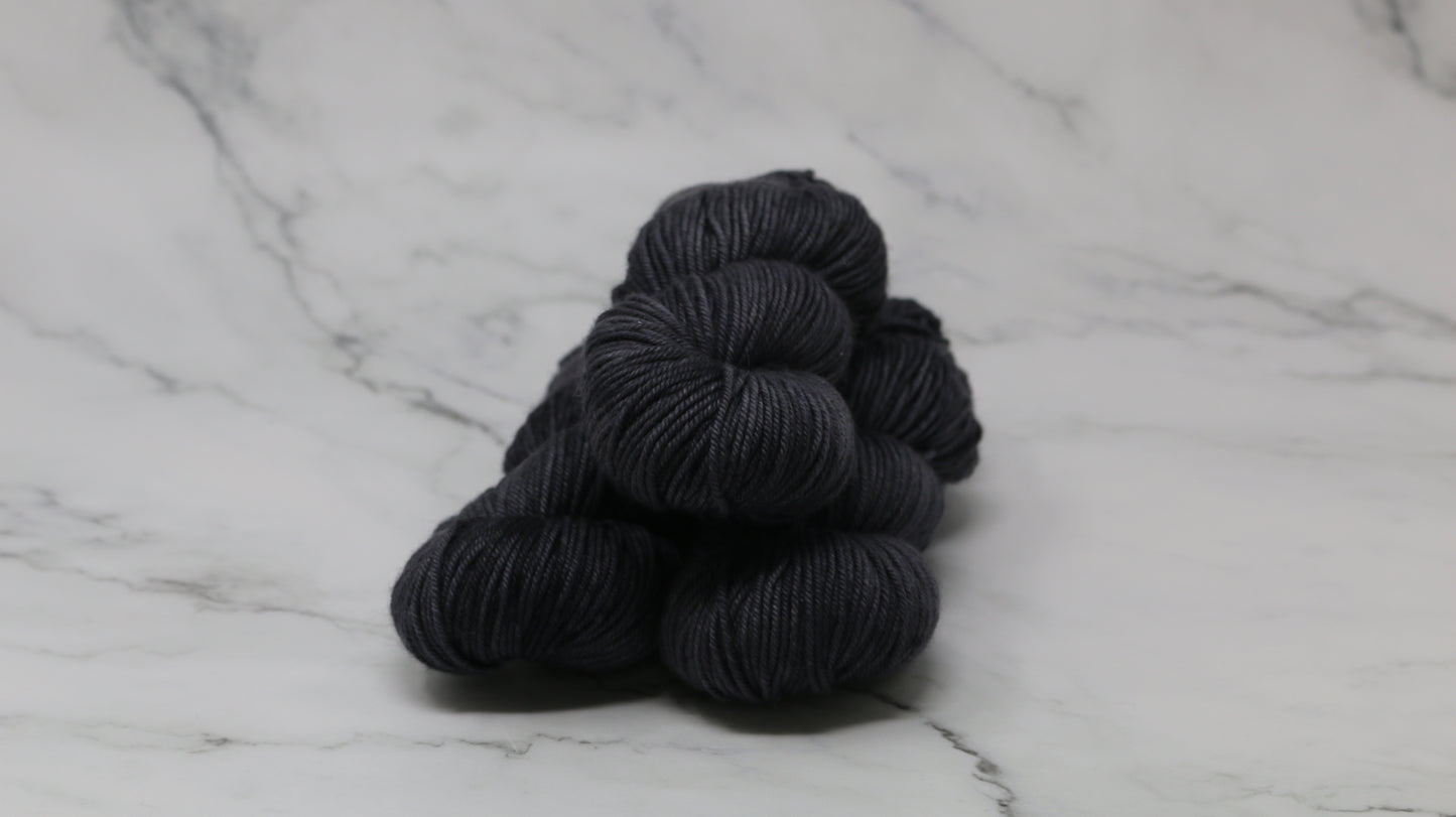 3 skeins of dark grey yarn on a marble surface and background