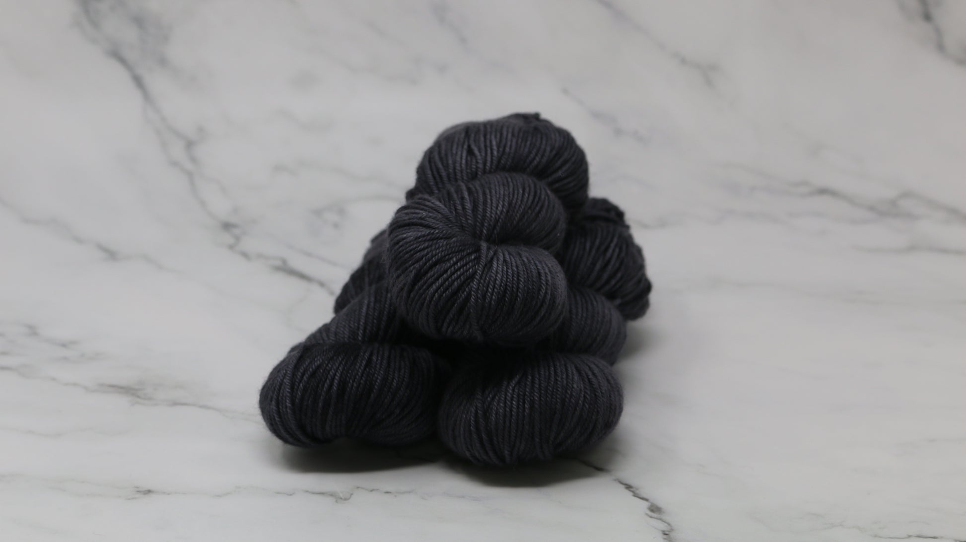 3 skeins of dark grey yarn on a marble surface and background