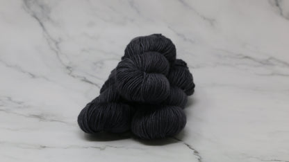 3 skeins of dark grey yarn on a marble surface and background