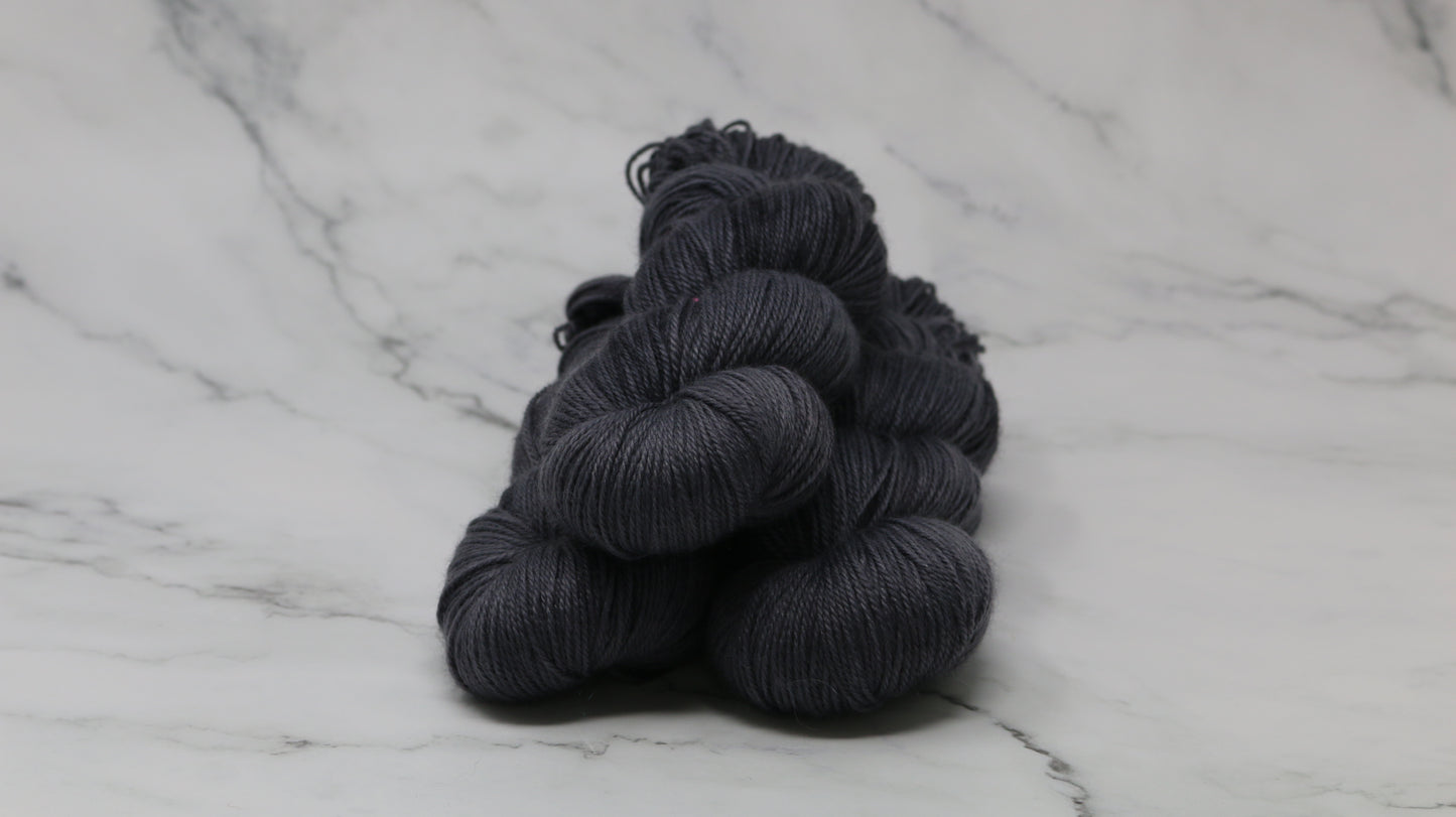 3 skeins of dark grey yarn on a white marble surface and background