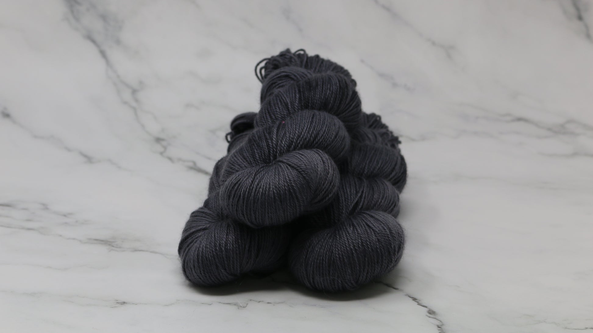3 skeins of dark grey yarn on a white marble surface and background