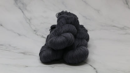 3 skeins of dark grey yarn on a white marble surface and background