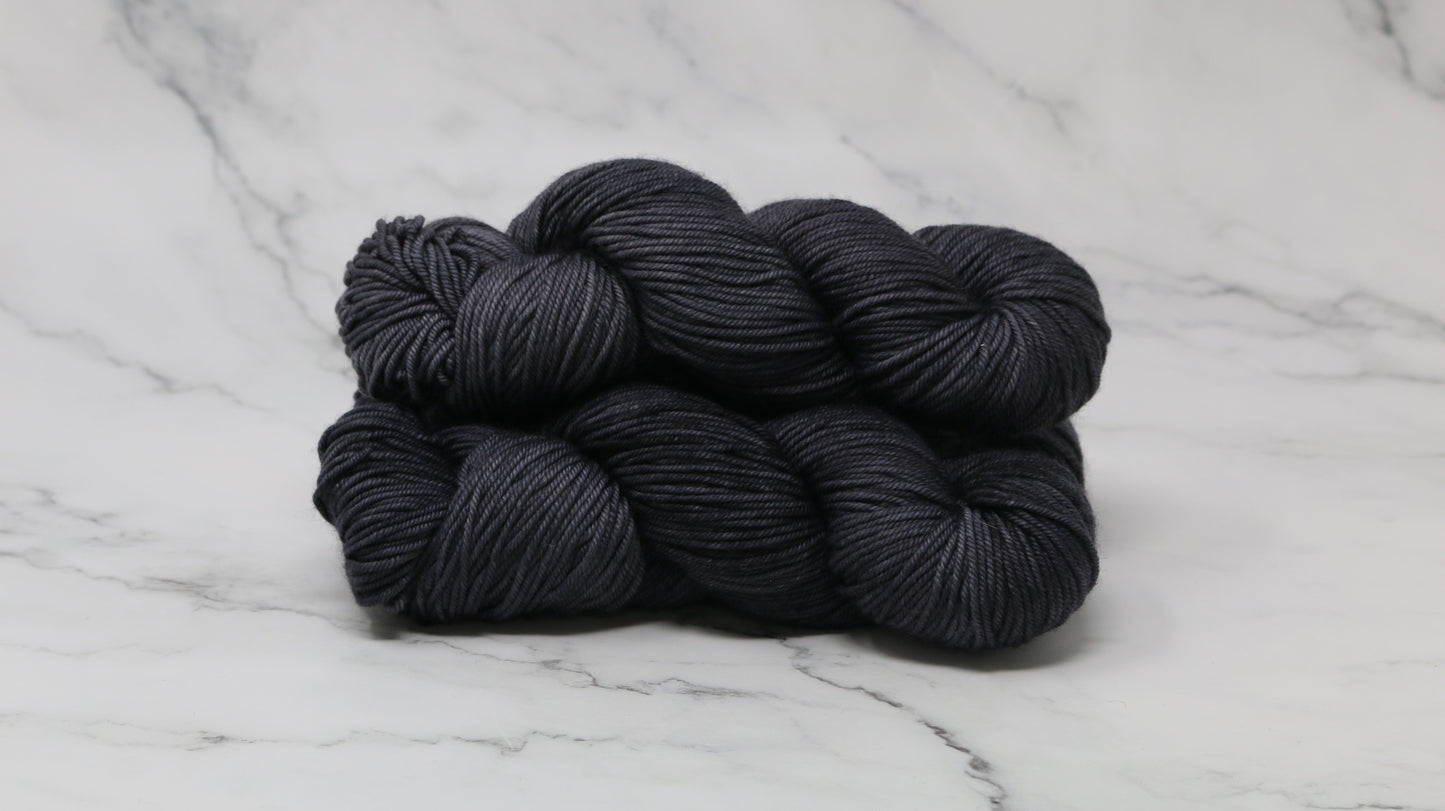 3 skeins of dark grey yarn on a marble surface and background
