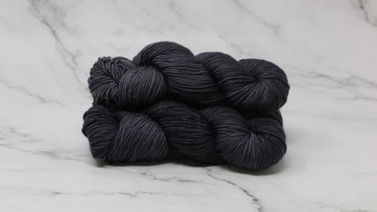 3 skeins of dark grey yarn on a marble surface and background