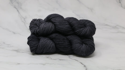 3 skeins of dark grey yarn on a marble surface and background