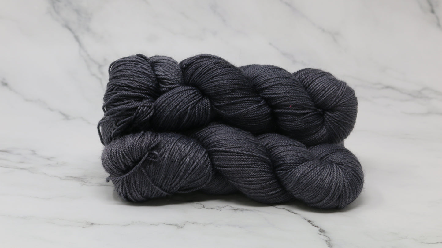 3 skeins of dark grey yarn on a white marble surface and background