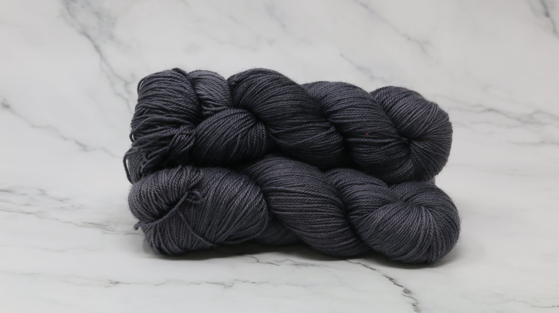 3 skeins of dark grey yarn on a white marble surface and background