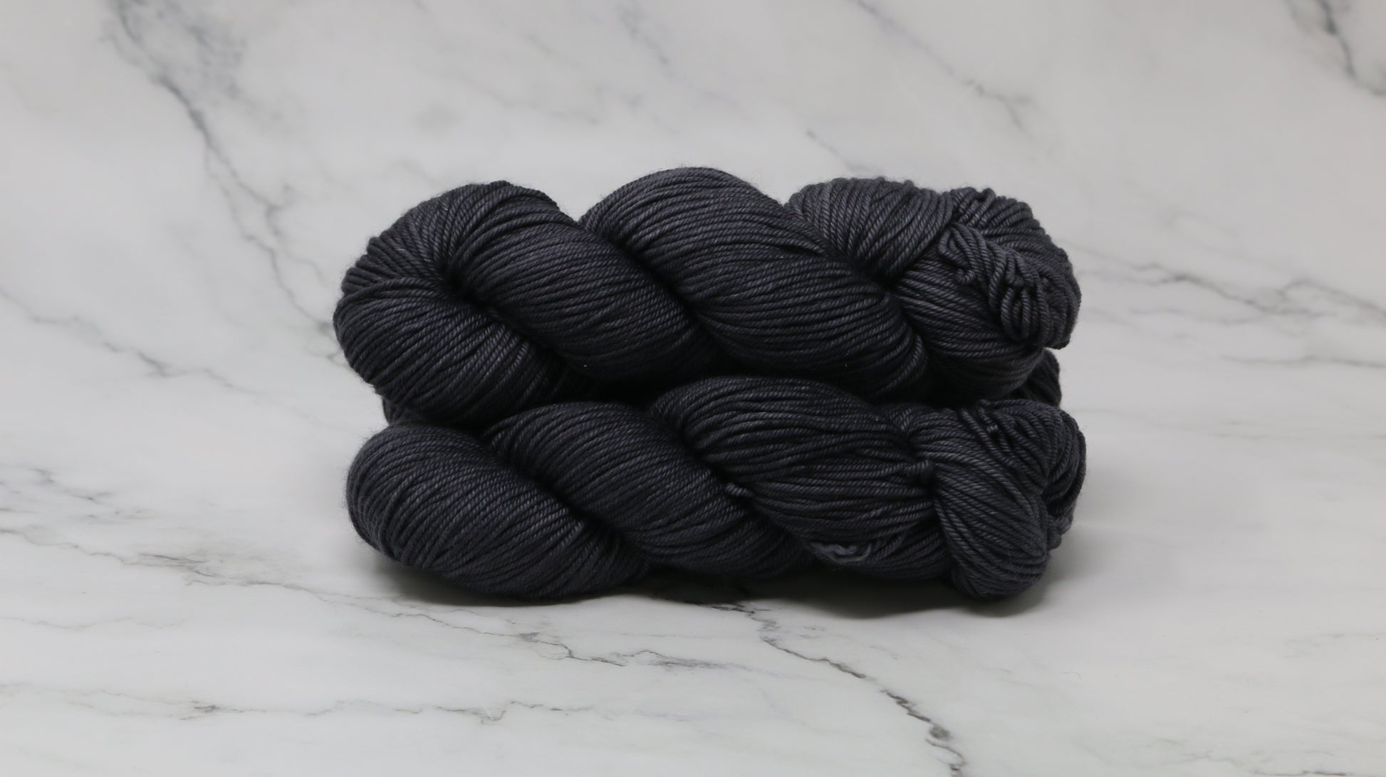 3 skeins of dark grey yarn on a marble surface and background