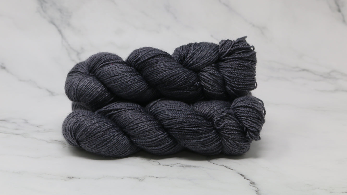3 skeins of dark grey yarn on a white marble surface and background