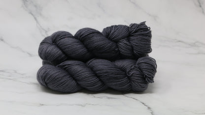 3 skeins of dark grey yarn on a white marble surface and background