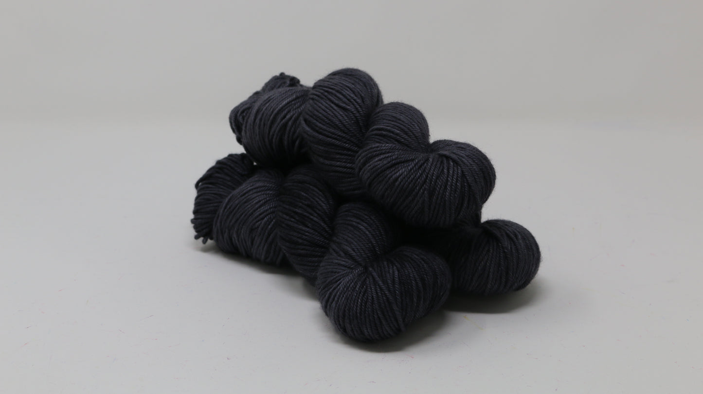 3 skeins of dark grey yarn on a white surface and background