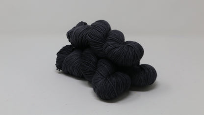 3 skeins of dark grey yarn on a white surface and background