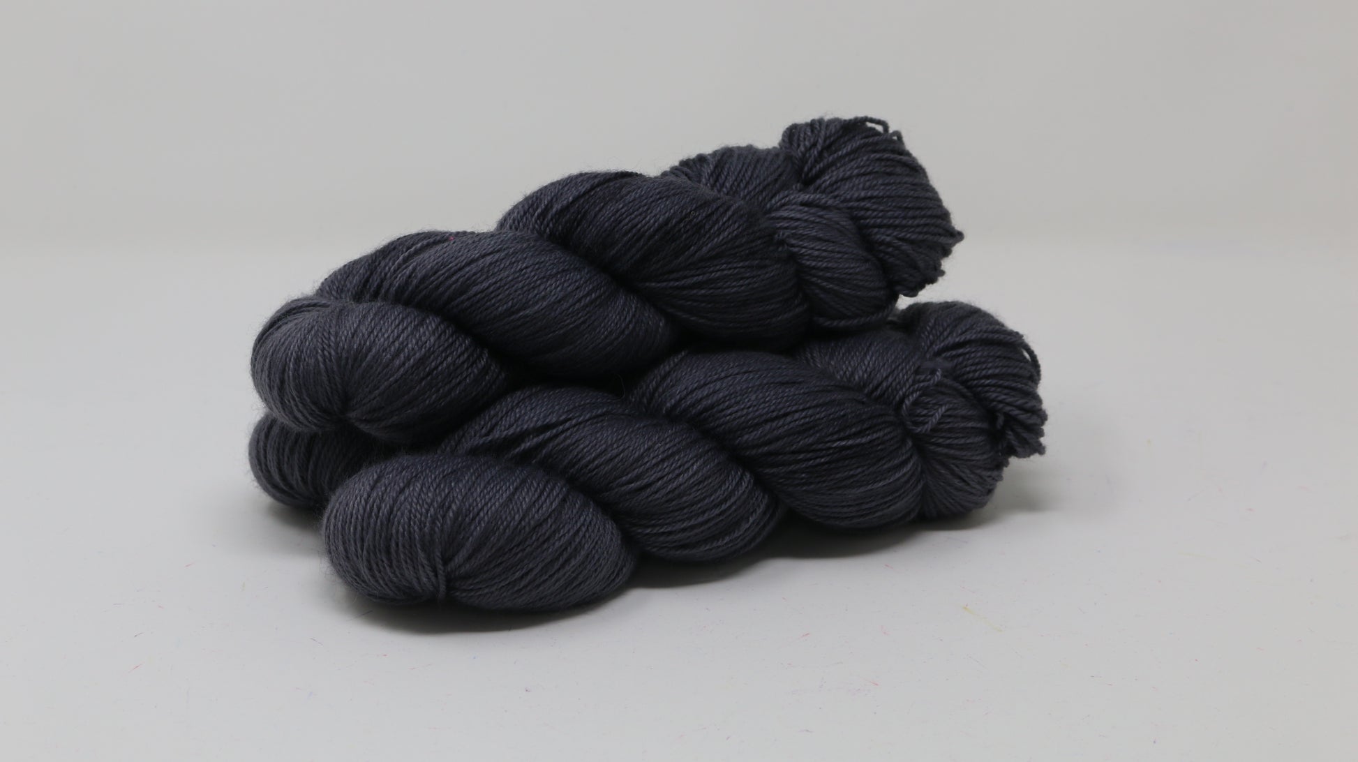 3 skeins of dark grey yarn on a white surface and background