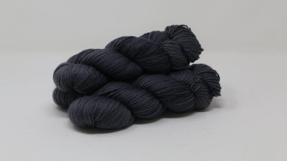3 skeins of dark grey yarn on a white surface and background