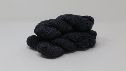 3 skeins of dark grey yarn on a white surface and background