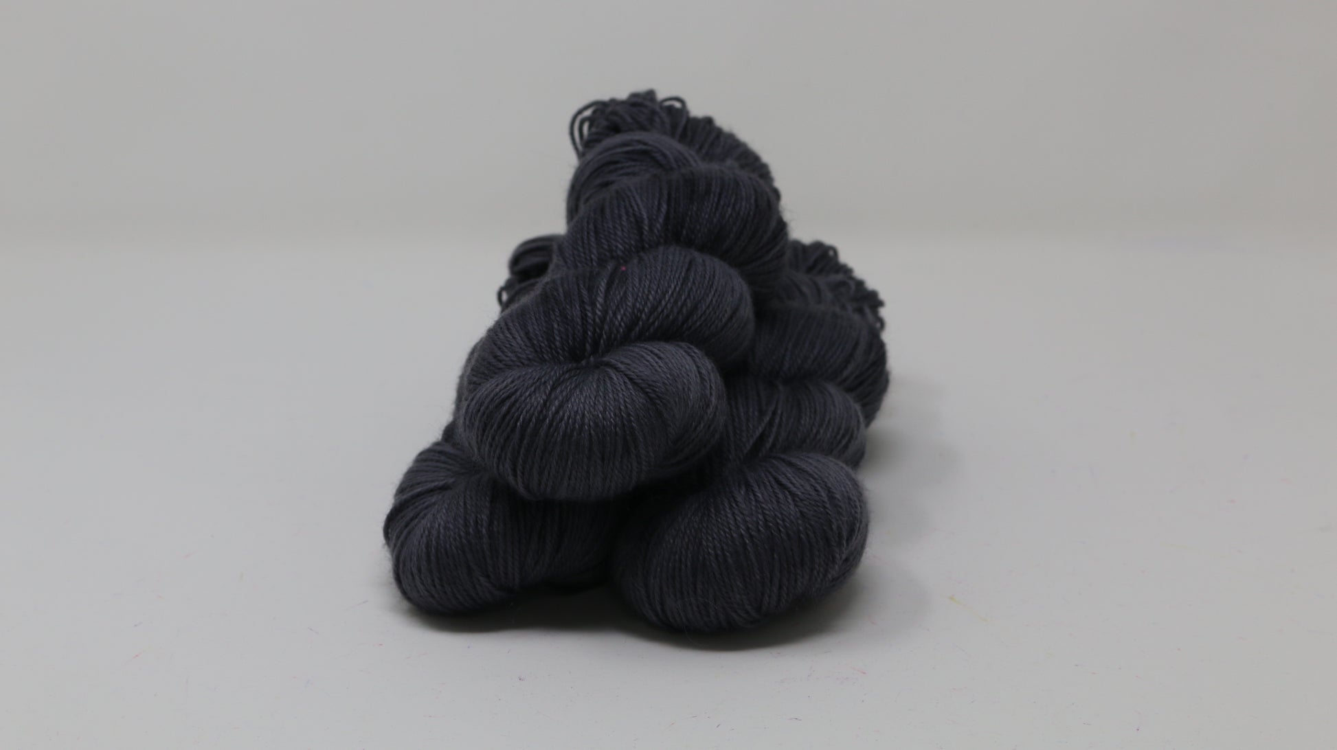 3 skeins of dark grey yarn on a white surface and background