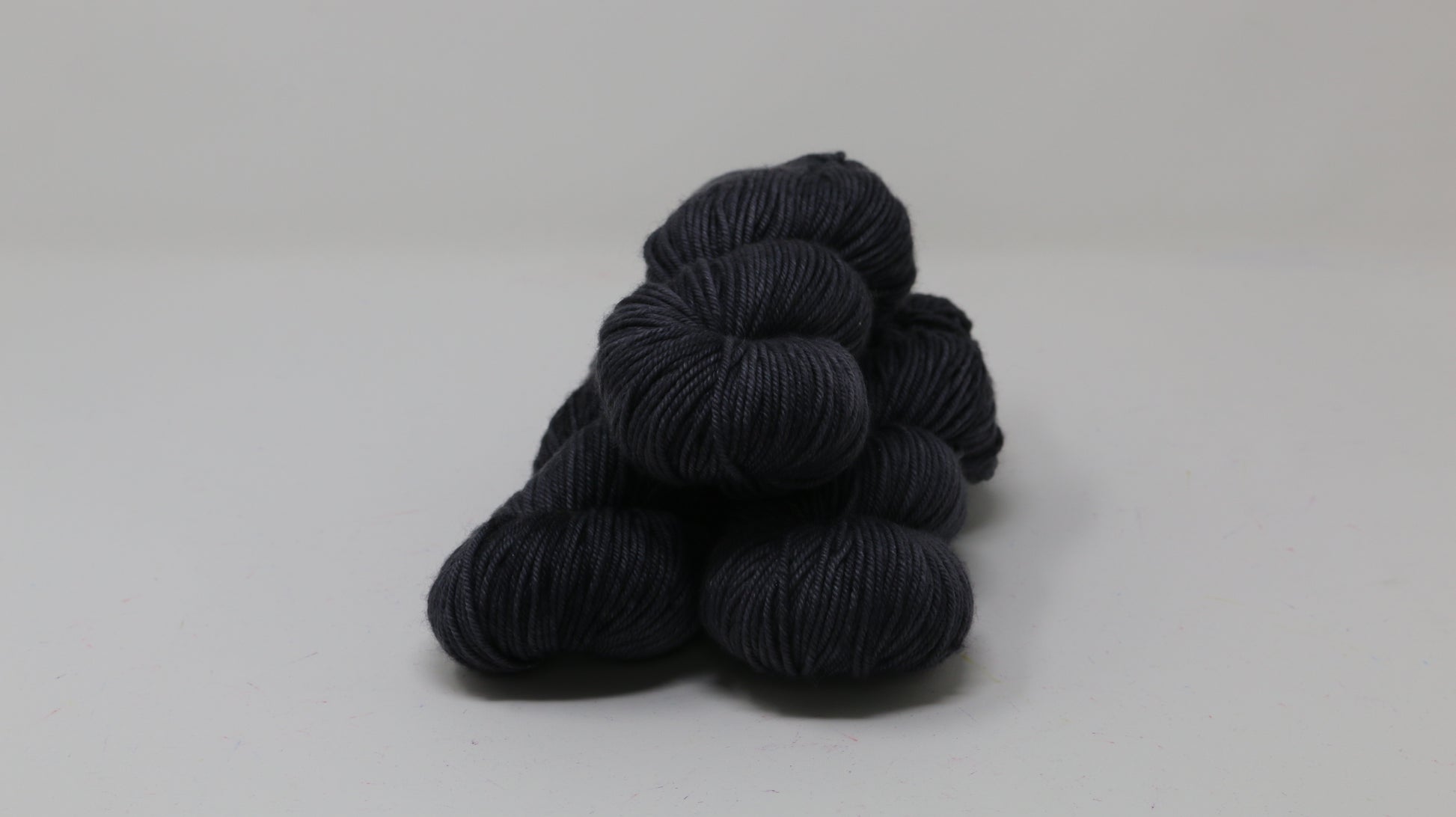 3 skeins of dark grey yarn on a white surface and background