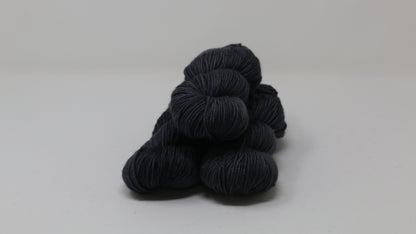 3 skeins of dark grey yarn on a white surface and background