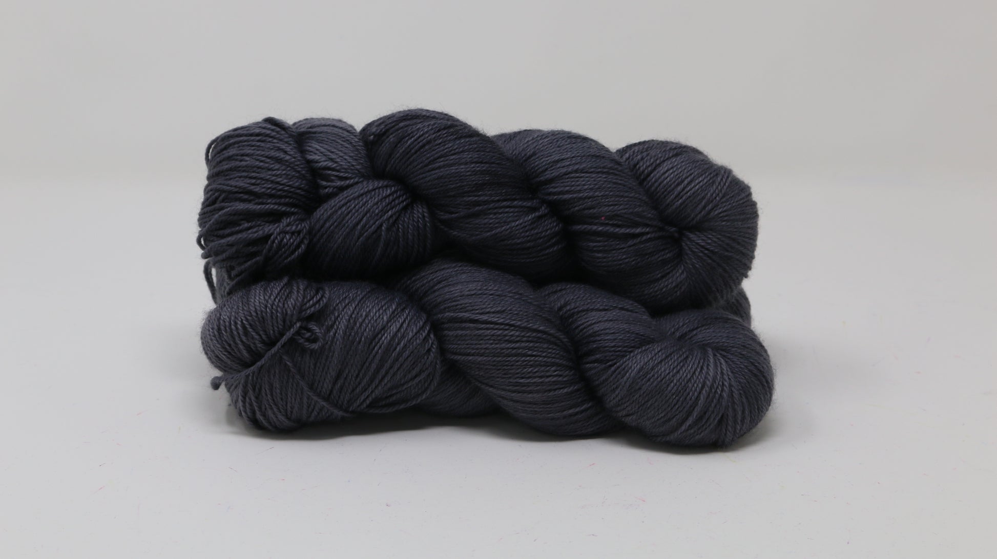 3 skeins of dark grey yarn on a white surface and background