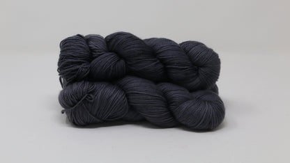 3 skeins of dark grey yarn on a white surface and background