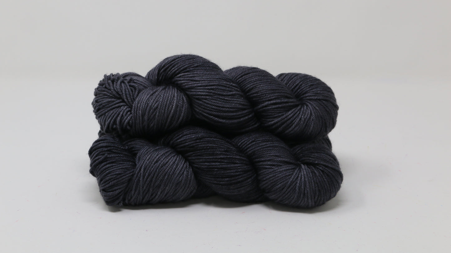 3 skeins of dark grey yarn on a white surface and background